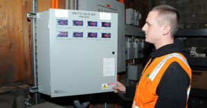 man in orange vest looking at an industrial freezer control station