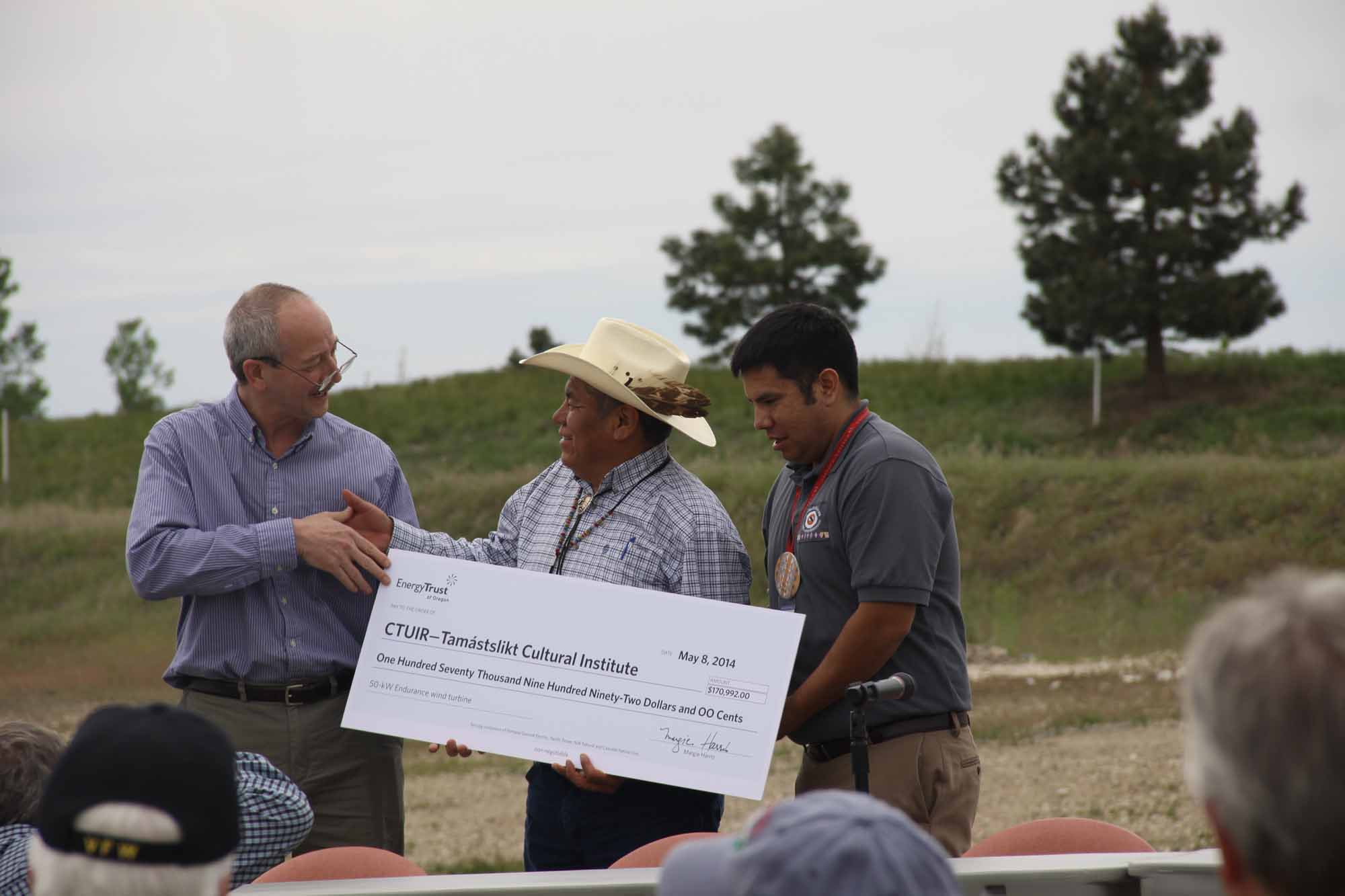 Energy Trust employee giving a "big check" to Chairman Gary Burke and Treasurer Aaron Hines of the Confederated Tribes of the Umatilla for their small wind turbine.