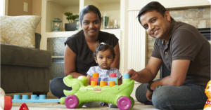 Couple with their small daughter sitting and playing on the floor of their home.