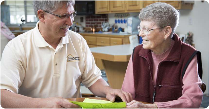 An employee from Home Comfort explains information to an elderly lady at her kitchen table.