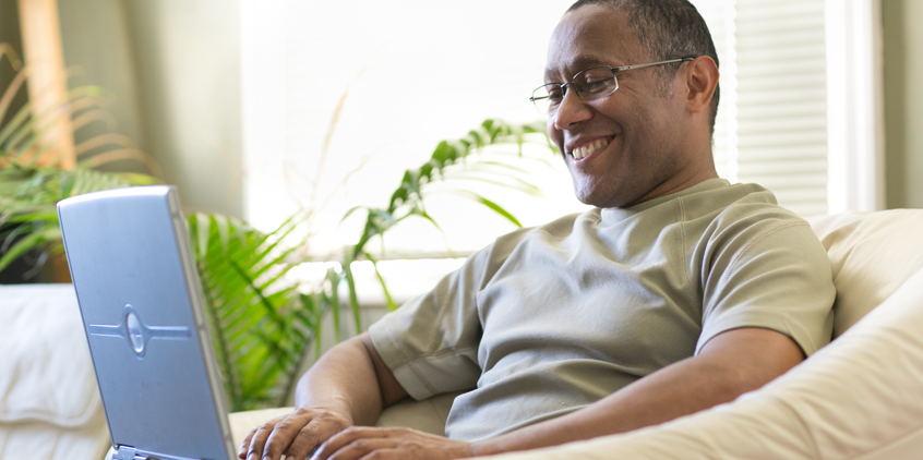 Man sitting on couch while working on a laptop.