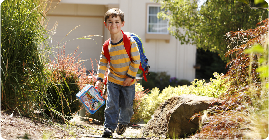 Little boy with his school backpack on and a lunch box in hand.