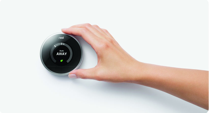 a smart thermostat mounted on the wall with a hand adjusting it