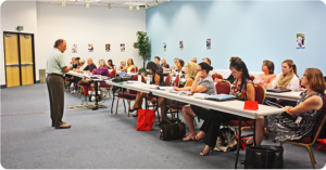 a speaker in front of a room full of people seated at tables