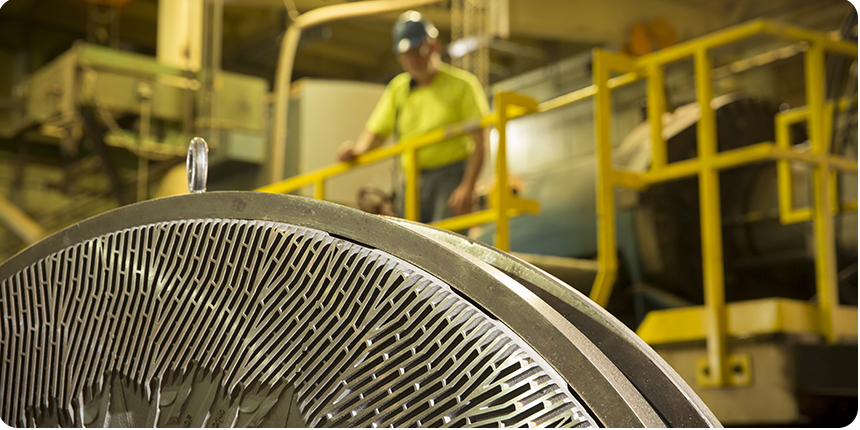 a close up of machinery with a man in a hardhat in the background.