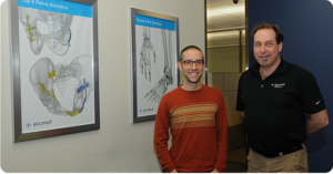 two men smiling infront of medical charts of bones