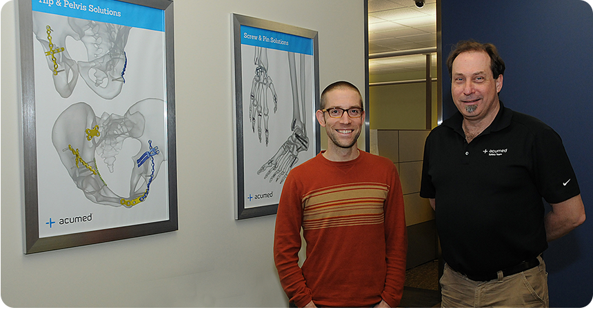 two men smiling infront of medical charts of bones