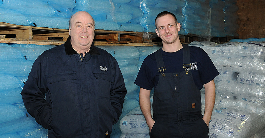 two men in blue standing infront of hundreds of bags of ice