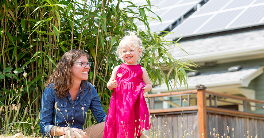 woman and smiling toddler in front of house with solar panels