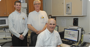 three men in matching company shirts in front of a computer