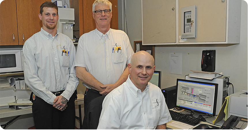 three men in matching company shirts in front of a computer