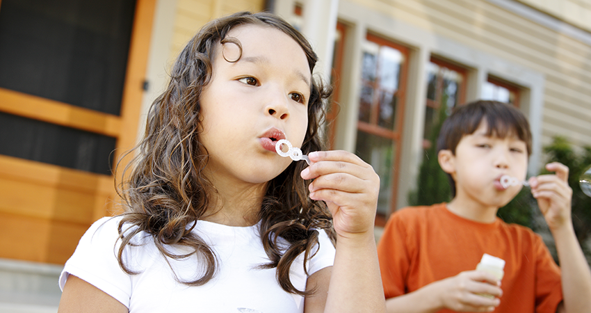 a boy and girl blowing bubbles in front of their home