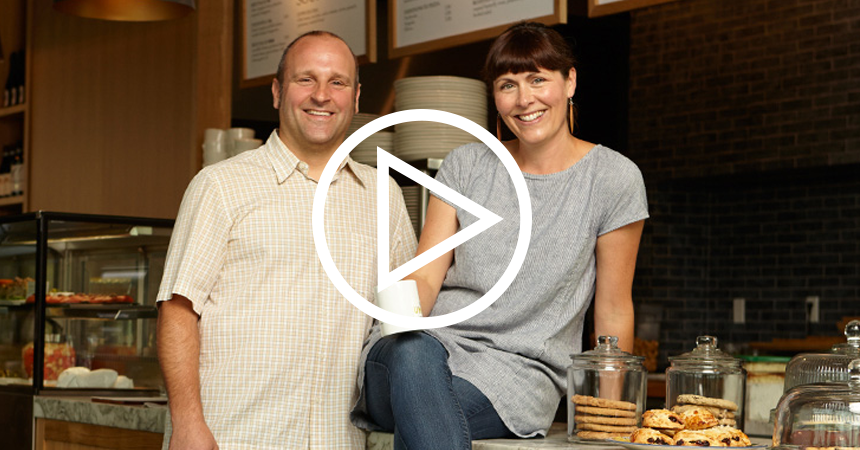 a smiling man and a smiling woman sitting on the counter of a restaurant