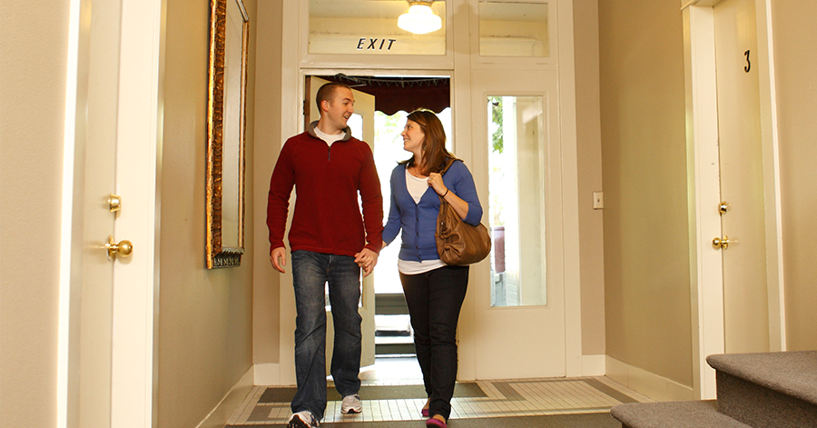 a man and woman walking into an apartment building holding hands