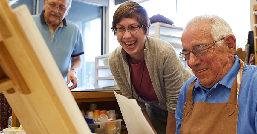 a laughing woman watching an elderly man painting