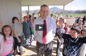 smiling school principal surrounded by waving students