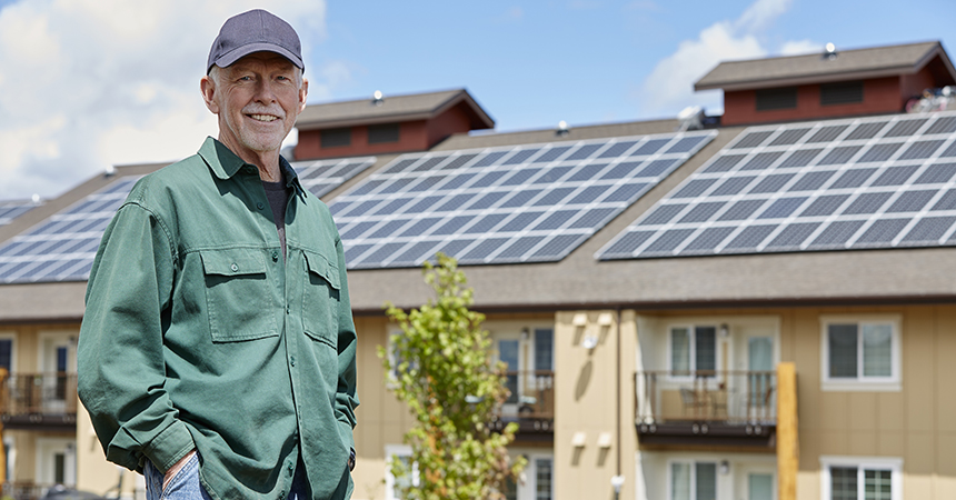 man in ballcap standing in front of multifamily building with solar panels on the roof