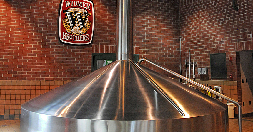 a large stainless steel vat in a brick building with the widmere logo in the background