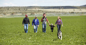 a family walking across a farm field with a dog and two children