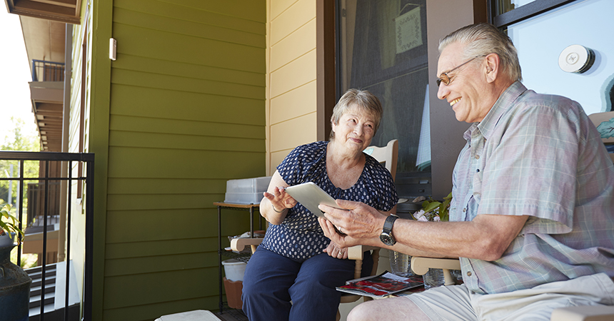 a smiling elderly couple looking at an ipad together on their porch
