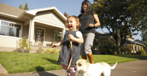 smiling woman and toddler walking a dog in front of their house