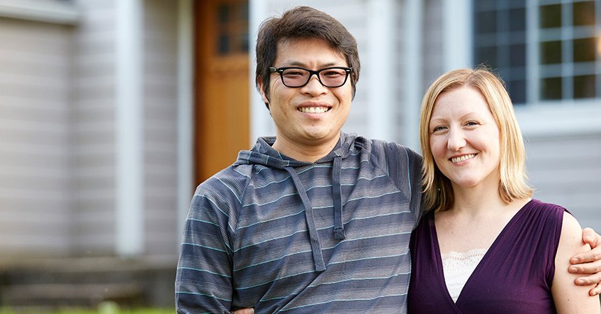 smiling man and woman standing in front of their home