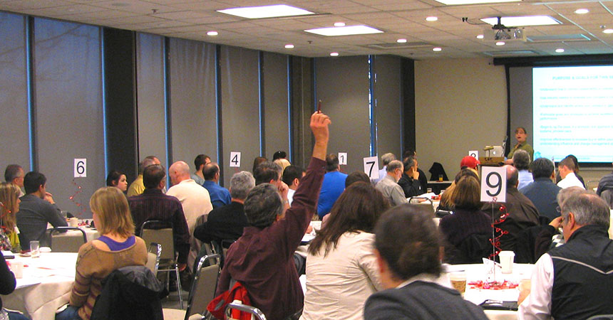 large training room filled, a man with a raised hand asking the speaker a question