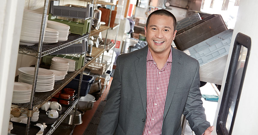 Smiling man standing in the kitchen of a restaurant.