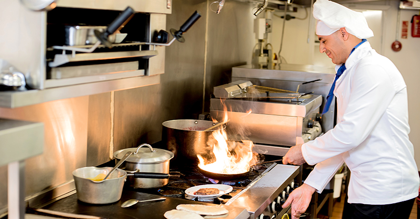 Chef standing at stove top holding a pan with flames arising out of it.