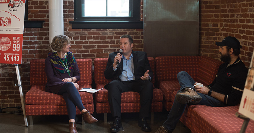 People sitting on red couches listening to a man talking into a microphone.