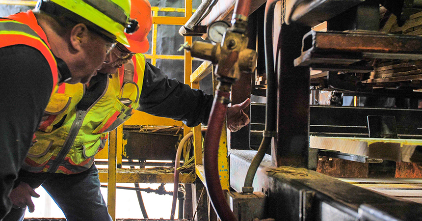 Two men in hard harts examining a gauge on a large hose