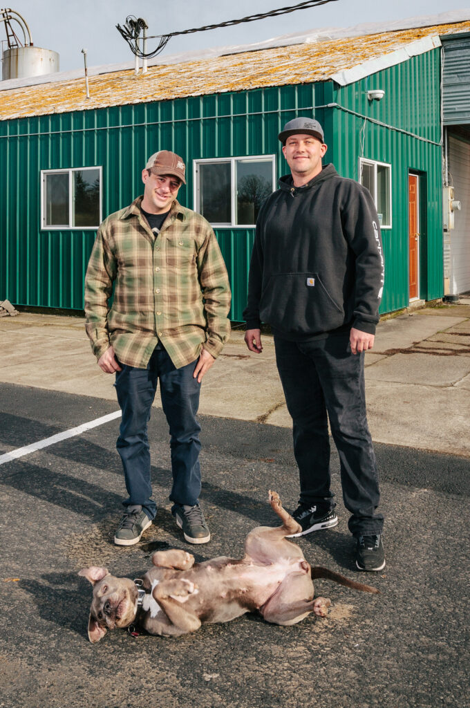 Two men and a dog in front of an Eco Firma building