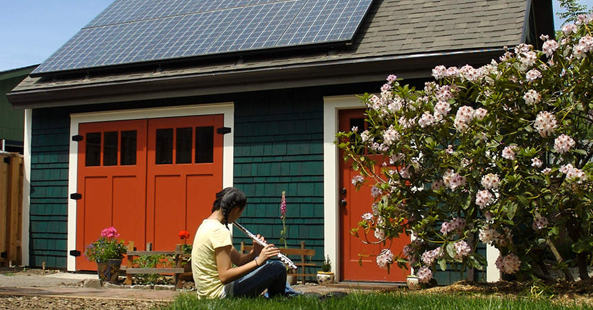 young woman playing flute in front of a solar paneled garage