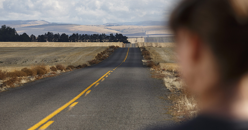 woman staring down a very straight road in the countryside