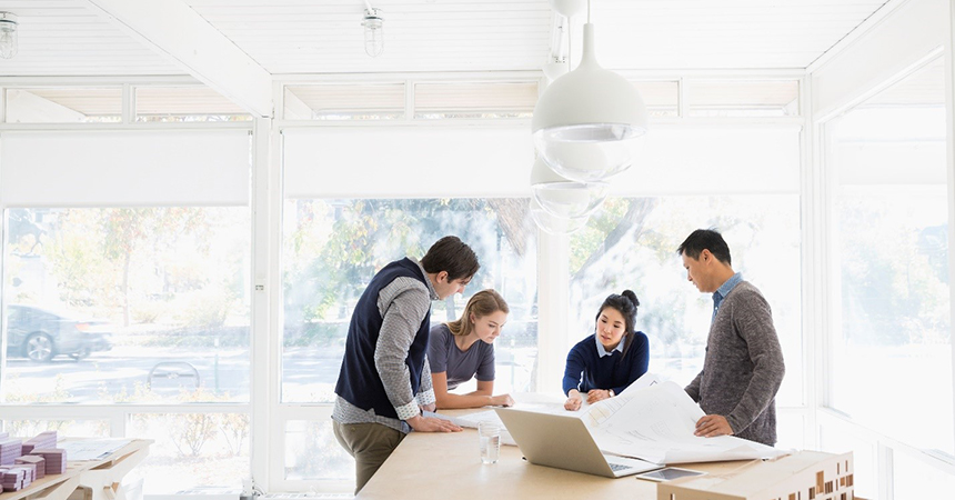 four people examing blue prints in a room filled with natural light