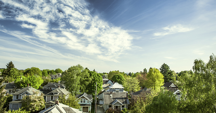 Portland Oregon's east-side "suburbs" on a warm summer day, a vibrant blue sky and clouds over neighborhood houses and green trees. Horizontal with copy space.