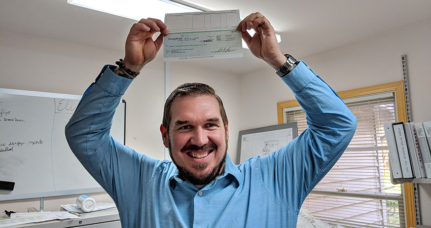 A smiling man holds up a check with his incentive
