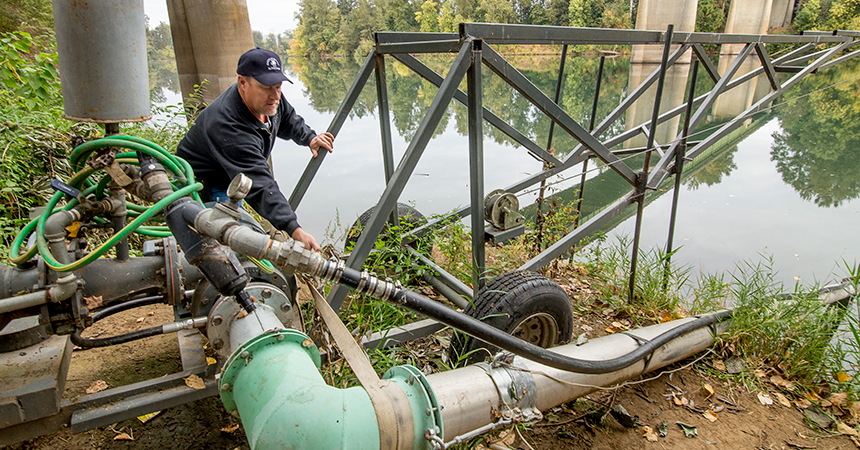 Man adjusting a pump along the banks of a river.