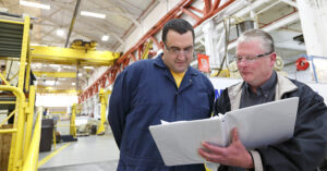 Two men overviewing documents in a well lit warehouse