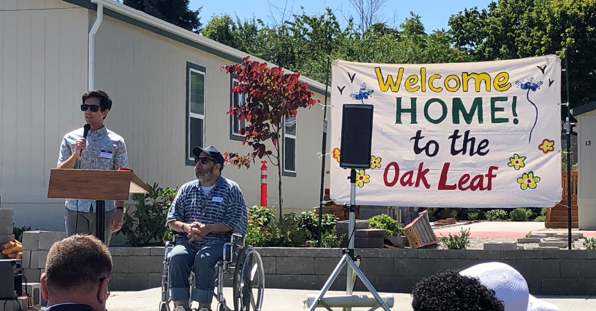 a welcome home to oak leaf banner with a man at a podium and a man in a wheelchair addressing a crowd