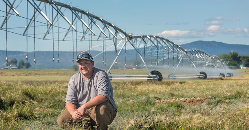 Man kneeling in a field with a pivot system behind him.