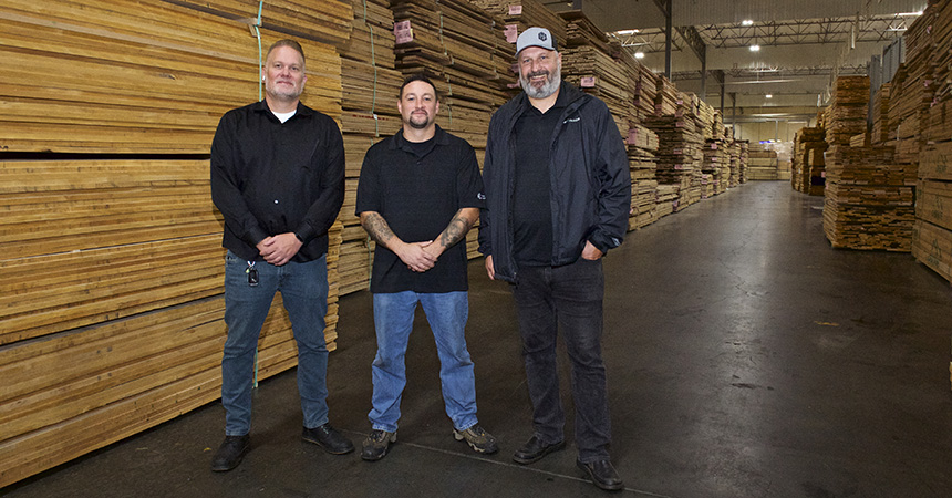 three men standing among rows and rows of lumber