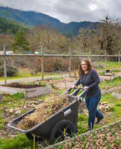 A woman pushing a wheelbarrow in a garden area.