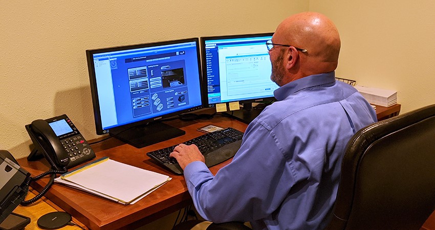 a man sitting at a desk with two computer monitors 