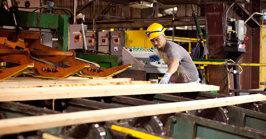 A man in a hard hat working on lumbar in a lumberyard