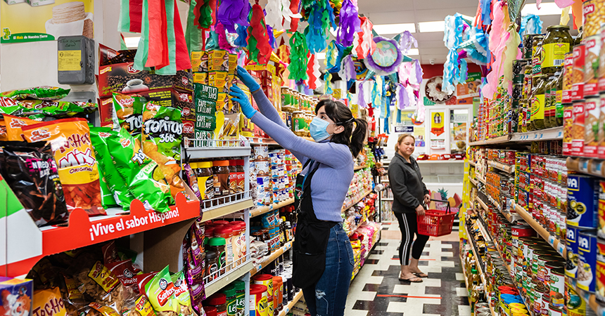 a woman in a mask stocking a grocery store shelf