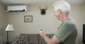 a man with white hair adjusting his heat pump with a remote control