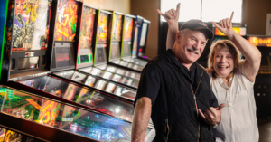 Woman making celebratory hand gestures behind man near a bank of pinball machines