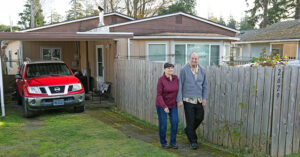Man and woman smiling as they walk outside their home along a fence line.