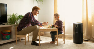 Man and child sit at small table playing with toys while an air purifier works nearby.